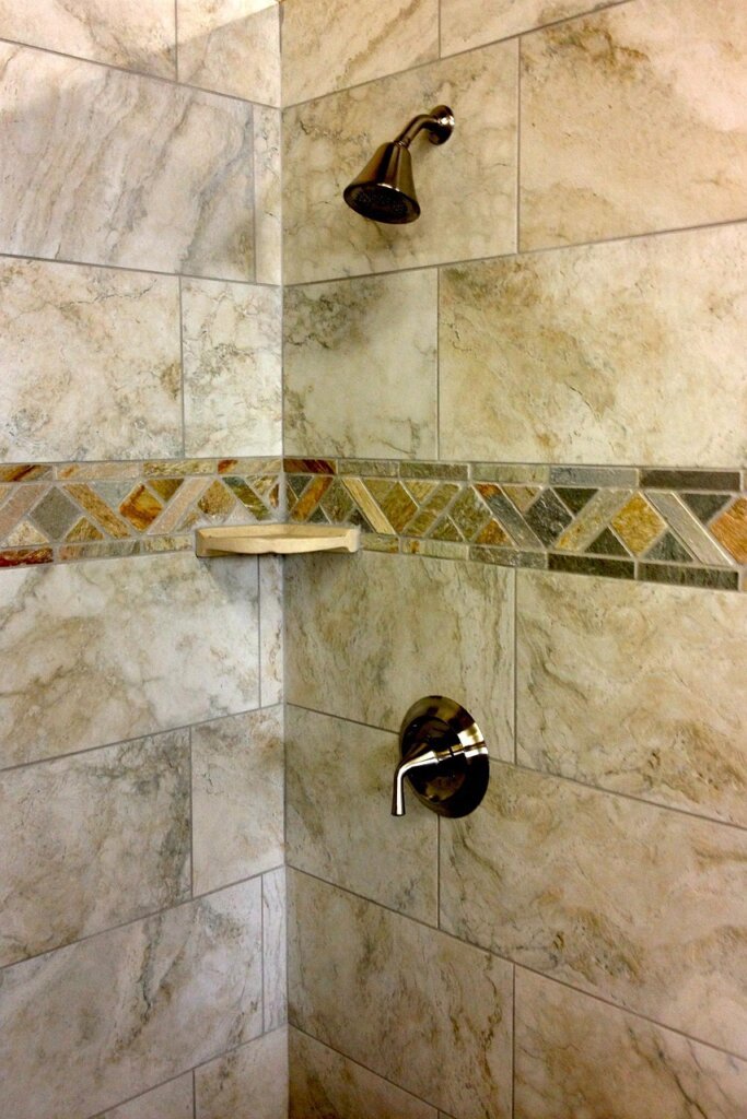 person wiping bathroom tiles with squeegee after shower