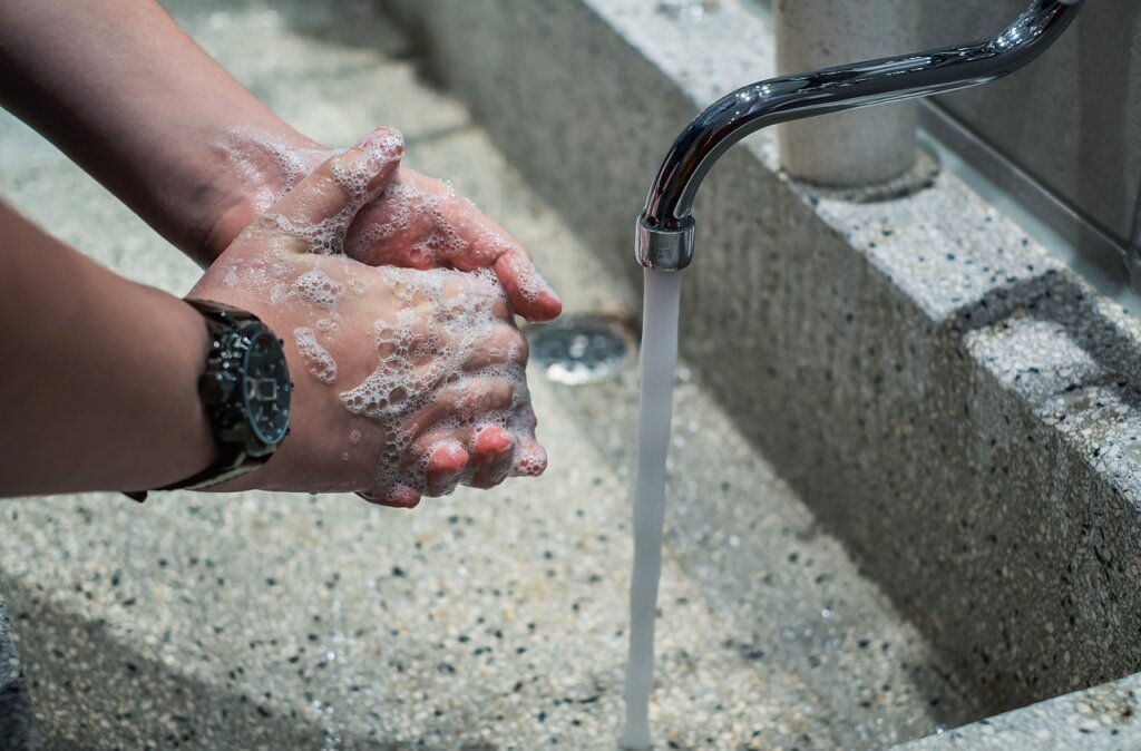 woman rinsing air conditioner filter under running water in bathroom sink