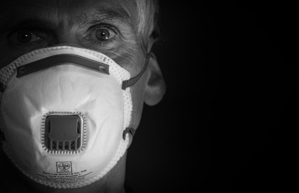 person wearing N95 mask and gloves scrubbing mold off wallpaper