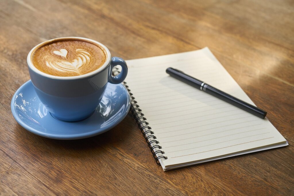 checklist notebook with pen and coffee cup on desk